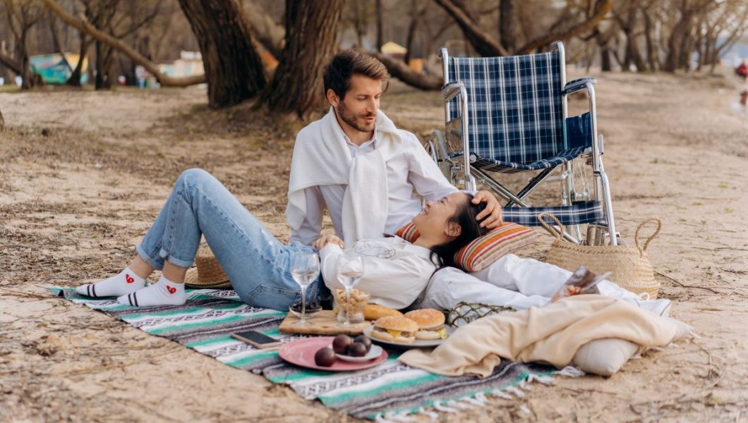 Disabled lovers have picnic on the beach next to wheelchair